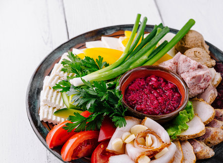 Horseradish sauce standing on a appetizers platter with salo, sausage and vegetables on white wooden tableの写真素材