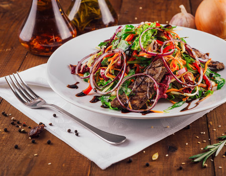Warm salad with grilled beef and fresh vegetables seasoned with balsamic sauce, served on white plateの写真素材