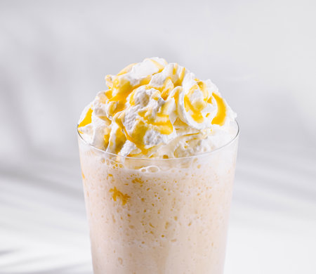 Caramel being poured on a delicious frappuccino with whipped cream in a tall glass