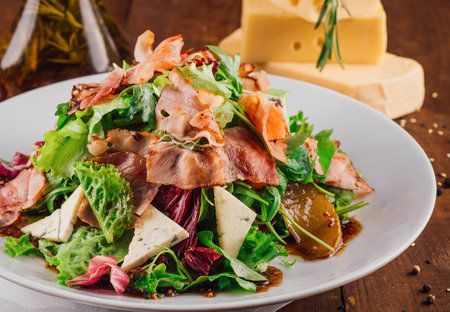 Fresh salad with jamon, pear and dor blue cheese seasoned with oil and herbs sauce served on white plateの写真素材