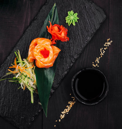 Delicious salmon sashimi appetizer served on black slate with wasabi, pickled ginger, soy sauce and white flowerの写真素材