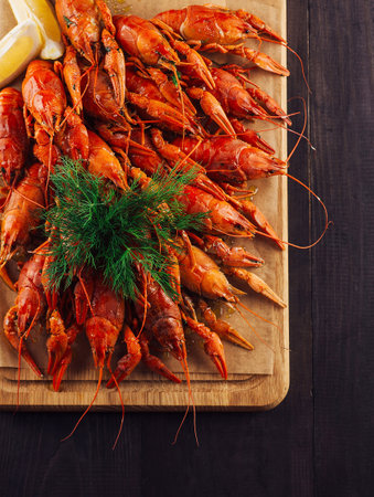 Boiled crayfish decorated with dill and lemon slices lying on the wooden boardの写真素材