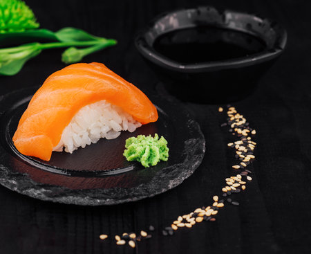 Salmon nigiri sushi served with wasabi paste and soy sauce resting on a black slate plateの写真素材