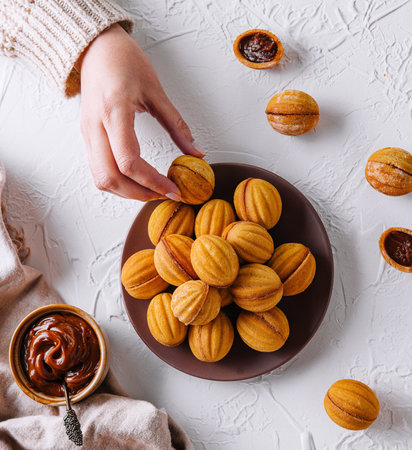 Overhead view of a woman's hand picking a cookie from a plate full of delicious walnut-shaped treatsの写真素材