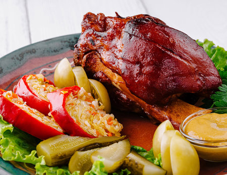 Delicious roasted pork knuckle is served on a plate with sauerkraut, pickles, and mustardの写真素材