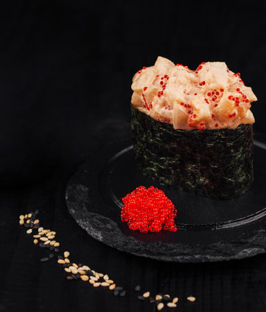 Spicy gunkan maki sushi with tobiko and spicy sauce standing on black stone plate decorated with sesame seedsの写真素材