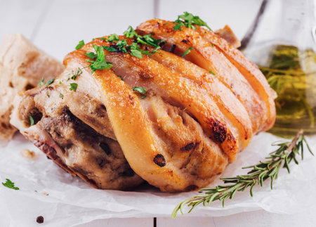 Juicy and flavorful pork knuckle is lying on white baking paper, decorated with fresh rosemary and spicesの写真素材