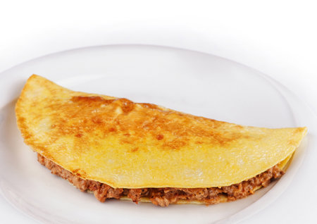 Delicious omelette filled with minced meat is lying on a white plate on a white backgroundの写真素材