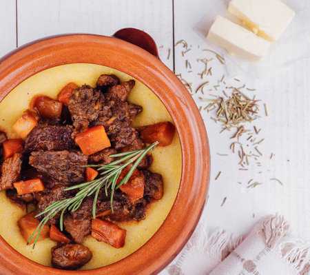 Delicious beef stew with polenta and vegetables in a rustic earthenware dish, garnished with rosemaryの写真素材