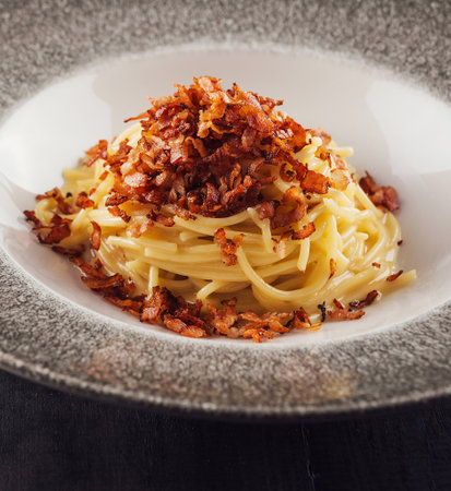 Delicious spaghetti carbonara topped with crispy bacon bits, served on a modern plateの写真素材