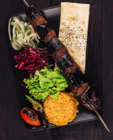 Eggplant kebab with minced meat, spices and vegetables served on black plate on dark wooden tableの写真素材