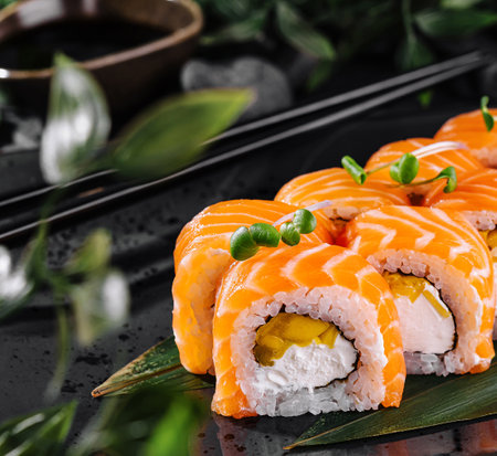 Gourmet salmon sushi rolls served on a black plate with garnishes, ready for a fine dining experienceの写真素材