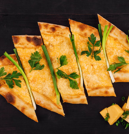 Turkish pide bread freshly baked with melted cheese and herbs, lying on a wooden table