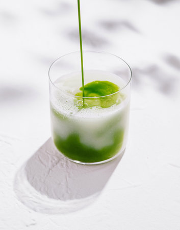 Barista is pouring a matcha latte into a glass, creating a refreshing and healthy beverageの写真素材