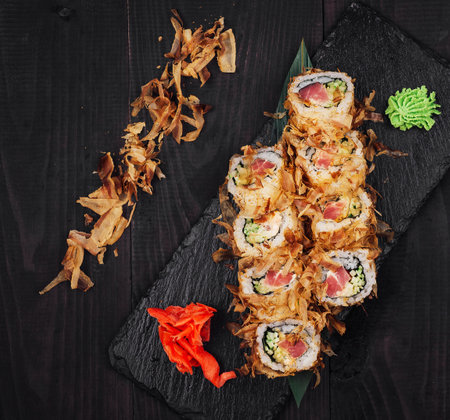 Sushi rolls set with tuna shavings served on black stone plate on dark wooden tableの写真素材