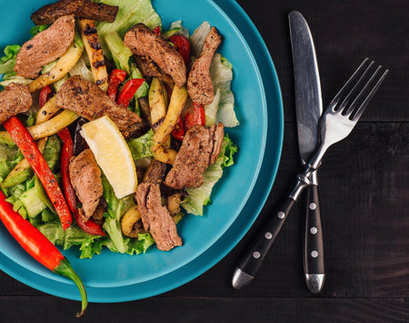 Warm salad with grilled veal, potatoes and peppers on dark wooden background, healthy food, top viewの写真素材