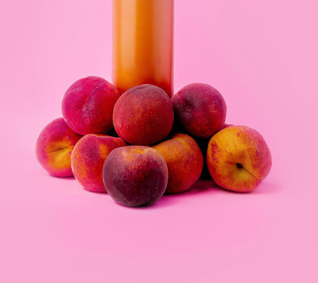 Ripe peaches gathered under a stream of peach juice, against a vibrant pink background, capturing the essence of summer freshnessの写真素材