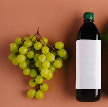 Fresh green grapes lying on a brown background near a bottle with a blank label, promoting healthy eating and natural beverage optionsの写真素材