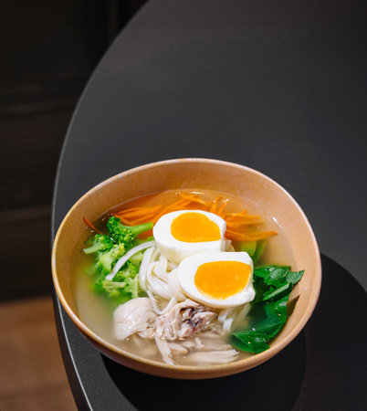 Savory chicken noodle soup with vegetables and eggs served in a modern restaurant setting