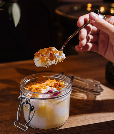 Woman holding a spoonful of dessert over a glass jar on a wooden tableの写真素材