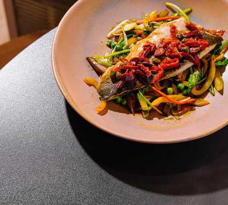 Grilled sea bass fillet served on a bed of sauteed vegetables, seasoned with herbs and spices, creating a visually appealing and flavorful dishの写真素材