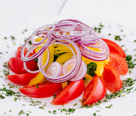 Fresh and vibrant salad featuring red onion, juicy tomato slices, and crisp bell pepper on a white plateの写真素材