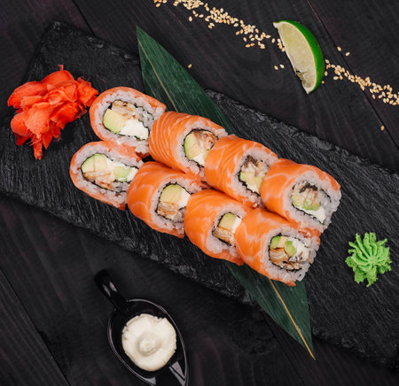 Philadelphia sushi rolls with salmon, avocado and cream cheese on black stone plate being served on...