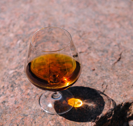 Glass of cognac is casting a long shadow on a rock on a bright sunny dayの写真素材