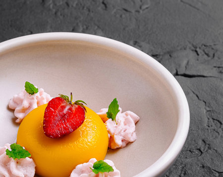 Mango panna cotta served on a white plate, decorated with a strawberry slice and drops of pink cream, on a dark backgroundの写真素材