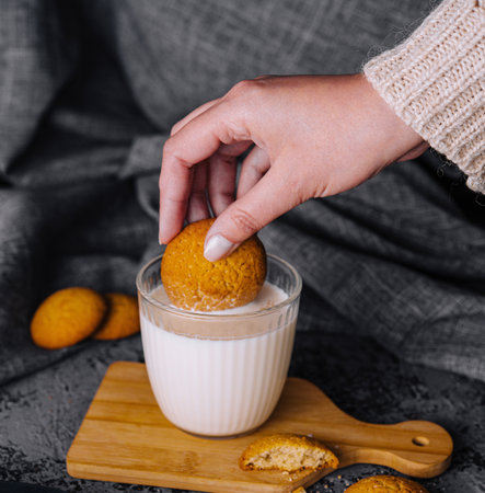 Hand is shown dipping a golden brown cookie into a glass of creamy milkの写真素材