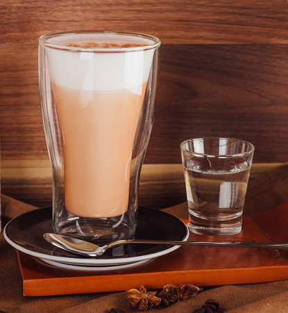 Latte coffee cup is standing on a wooden board with cocktail making equipment and a vase of lavender on a brown tableclothの写真素材