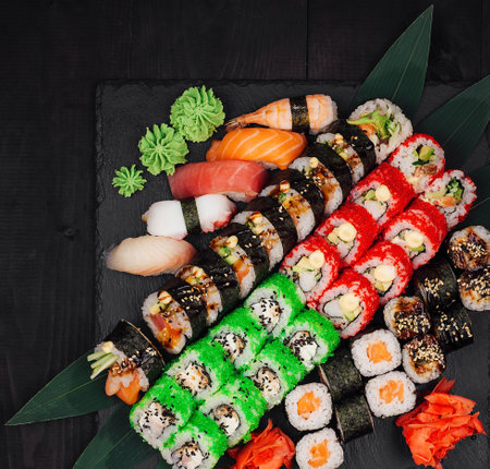 Different types of sushi are lying on a black stone tray decorated with bamboo leavesの写真素材