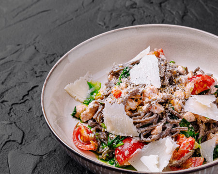 Black spaghetti with salmon, spinach, cherry tomatoes and parmesan lying on dark stone backgroundの写真素材