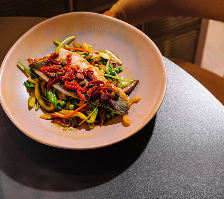 Grilled sea bass fillet served on a bed of sauteed vegetables, seasoned with herbs and spices,...