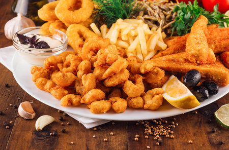 Large plate of delicious breaded seafood with french fries being served on wooden tableの写真素材