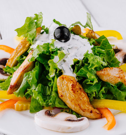 Fresh salad with lettuce, grilled chicken, mushrooms, bell peppers and white sauce dressing on a white plateの写真素材