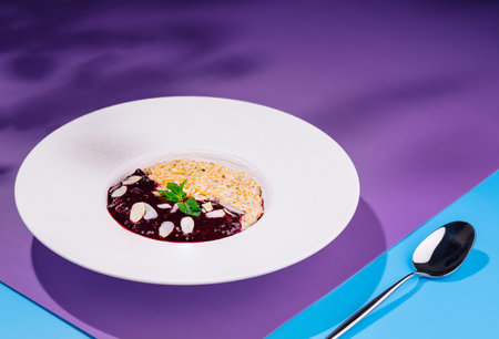 Oatmeal porridge is served on a white plate with berry jam, almond flakes and mint on a colorful backgroundの写真素材