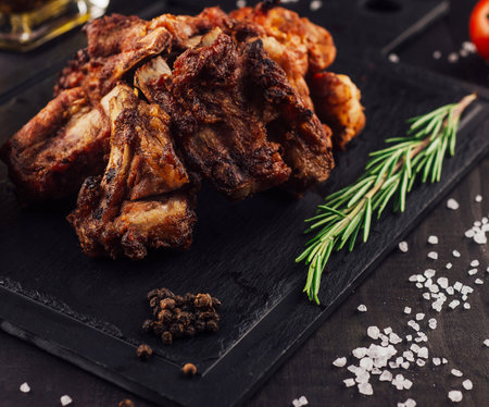 Delicious grilled pork ribs with a sprig of rosemary lying on a black stone boardの写真素材