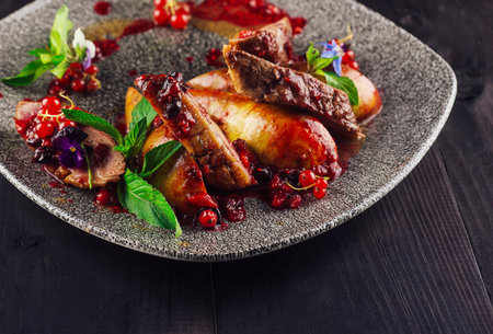 Sliced duck breast with berry sauce, pear, herbs and flowers, served on plateの写真素材