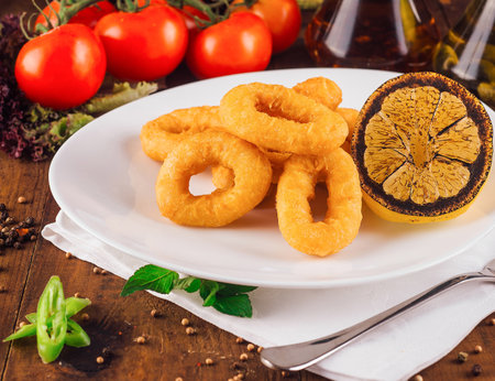 Delicious fried calamari rings served on white plate with grilled lemon and vegetables on rustic wooden tableの写真素材