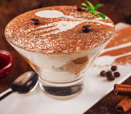 Delicious tiramisu dessert is being served on a white plate with coffee beans and cinnamon sticksの写真素材