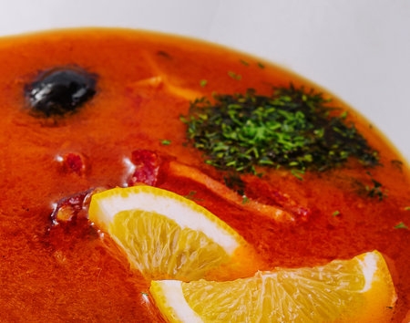 Zoomed-in view of a flavorful tomato soup garnished with lemon slices and fresh herbsの写真素材