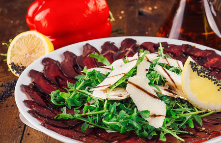 Sliced beef appetizer with arugula, parmesan cheese, lemon and balsamic vinegar arranged on a white plateの写真素材