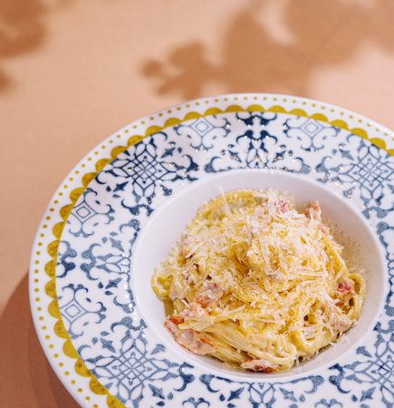 Appetizing plate of spaghetti carbonara garnished with cheese on a patterned plate, with a neutral backgroundの写真素材