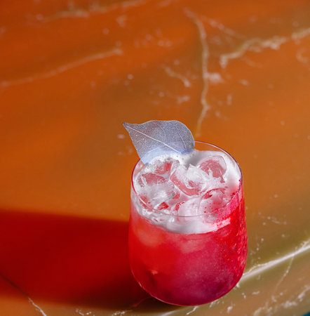 Red cocktail with ice and silver leaf garnish standing on a bar countertopの写真素材
