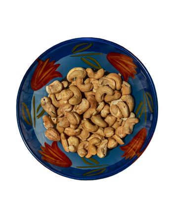 Roasted whole cashews in a glass blue bowl. Light brown nuts used as a snack. Seeds of Anacardium occidentale. Isolated macro photo close-up from above on a white background.の写真素材