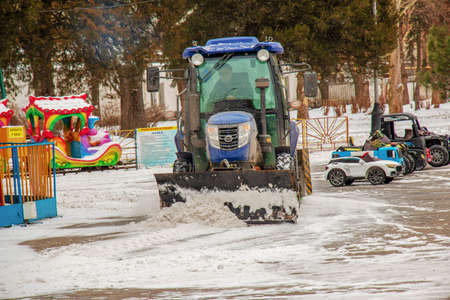 Dnipropetrovsk, Ukraine - 01.18.2022: A worker on a tractor removes snow in the city park.のeditorial素材