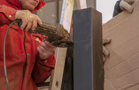 Dnepropetrovsk, Ukraine - 11.30.2021: A man cuts a metal profile on the street with an angle grinder. Sparks fly.のeditorial素材