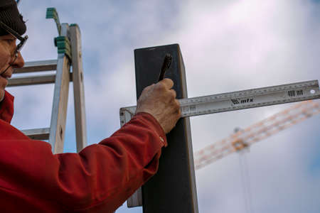 Dnepropetrovsk, Ukraine - 11.30.2021: A skilled worker measures and marks a line on a square pipe with an iron ruler for further cutting.のeditorial素材
