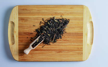 The tea is ready to be brewed. Spatula for brewing tea. Background of fragrant black tea leaves with lemongrass. Tea on a wooden board.の写真素材